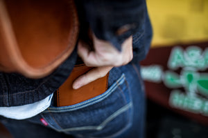 man putting leather bifold wallet into back pocket