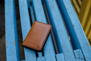 exterior view of brown leather vertical four pocket wallet sitting on blue bench