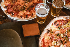 brown leather wallet displayed next to pizza and drink