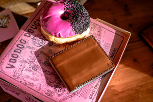 exterior view of brown leather bifold wallet next to pink donut
