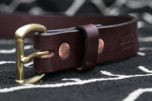 Macro shot of dark brown leather belt sitting on top of black blanket featuring solid copper rivets