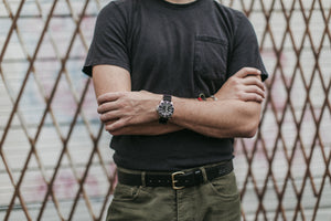 Adult male with crossed arms black shirt and green pants wearing a black leather belt and stainless watch
