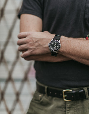 Adult male crossed arms wearing a stainless watch and black t-shirt with green pants