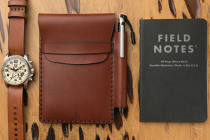 medium brown leather notebook wallet with pen sleeve next to analog watch