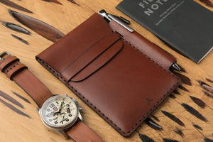 medium brown leather notebook wallet with pen sleeve next to analog watch