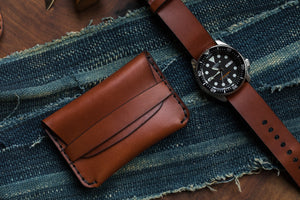 brown leather folding card wallet with leather closure next to leather watch strap