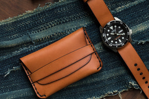 tan leather folding card wallet with leather closure next to matching watch strap