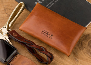 rear view of brown leather folding card wallet with brass nipple closure next to watch, keychain, and pen