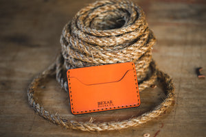 two pocket slim orange leather wallet next to twine rope