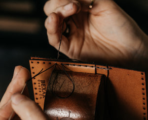 leather panels of bifold wallet being joined by thread in hands that are constructing wallet