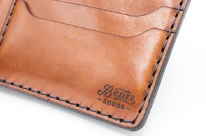 detail of logo engraved on blue cordovan and brown leather six pocket bifold wallet