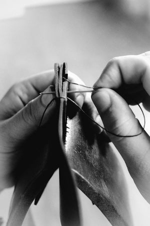 man handstitching leather wallet by pulling needle and thread