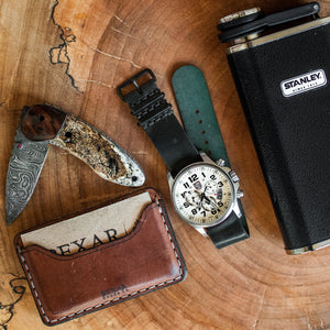 brown leather wallet with one card pocket, ID sleeve, and center divider next to leather watch strap and flask