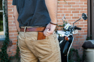man putting tan leather folding card wallet with leather closure into back pocket