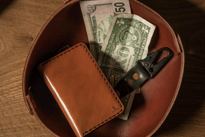 brown leather wallet inside leather valet tray also holding cash and keychain