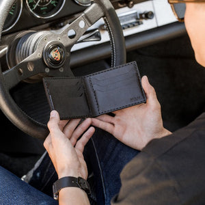man holding black leather six card pocket bifold wallet in sports car