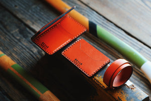 array of four pocket vertical orange leather wallet and other leather accessories next to axe
